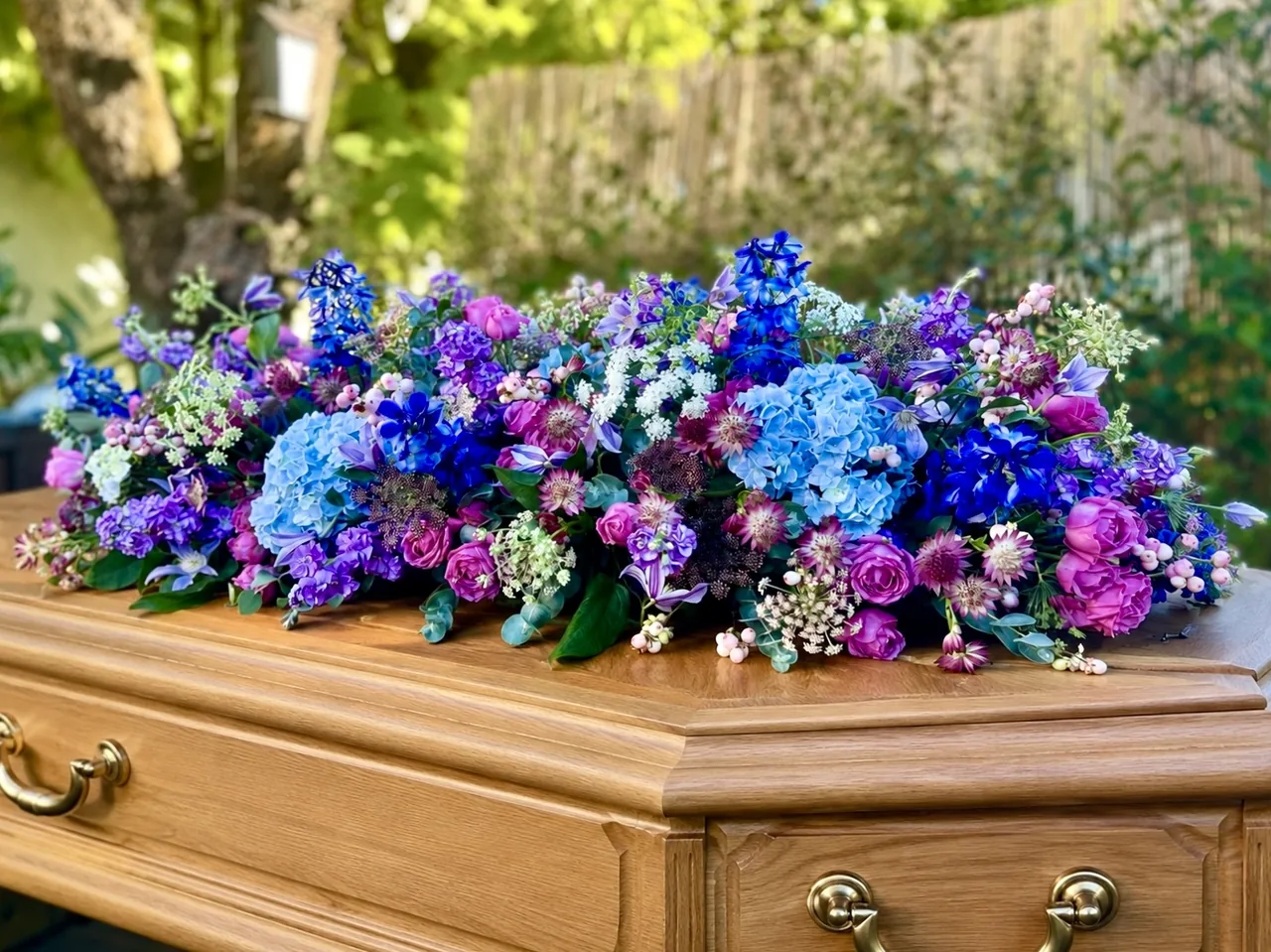 Dessus de cercueil composé de fleurs bleues, mauves et roses